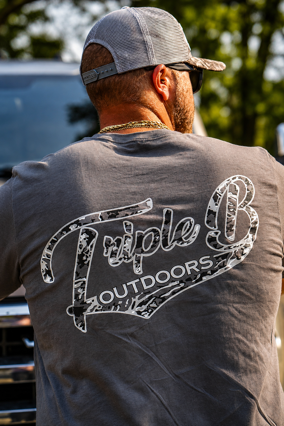 Zach Rushing wearing a bbb outdoors tshirt facing away from the camera, leaning on his truck